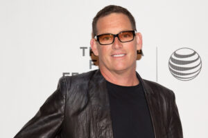 mike fleiss wearing sunglasses, a leather jacket and a black shirt at a red carpet event